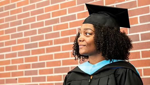 一个戴着毕业帽、穿着毕业服的女人站在砖墙前