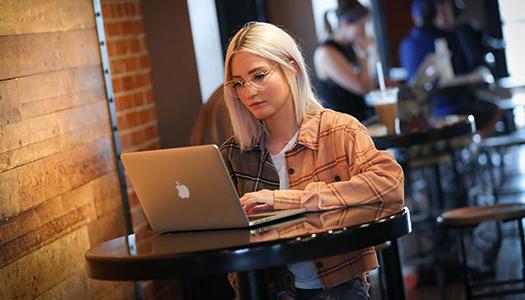 一位女士拿着笔记本电脑坐在咖啡店的桌子旁